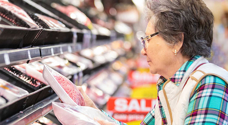 Elderly person comparing prices at grocery store.